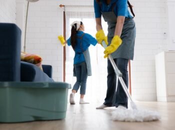 Two young women in uniform are cleaning the living room at home.