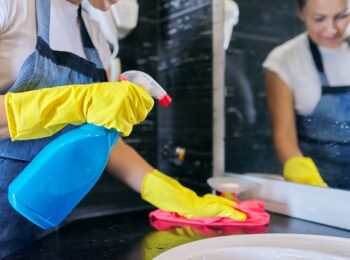 Cleaning the bathroom. Woman in apron gloves with detergent and microfiber cloth washing polishing wash basin, sanitary and hygiene in the house