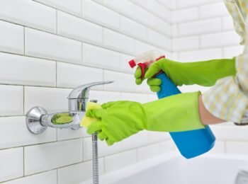 Cleaning the bathroom, a woman washing a tile wall and a mixer with a washcloth with detergent
