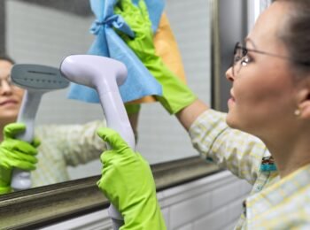 Woman doing cleaning in bathroom using vacuum cleaner, without use of household chemicals. Close-up of gloved hands with steam in the mirror, eco-friendly cleaning