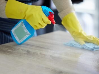 Hands, gloves and covid, spray cleaning table with disinfectant for risk prevention. Kitchen counte.