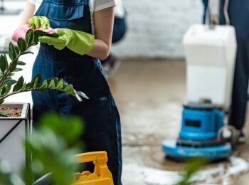 partial view of cleaner wiping office plants with rag near floor cleaning machine
