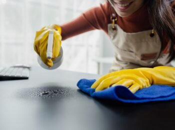 Cleaning desk surface in office with sanitizer spray, wear gloves and wipe the table with a towel, the housekeeper is cleaning the work desk for hygiene because of the Covid-19, cleaning idea.